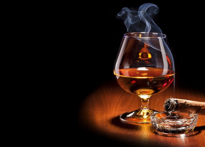 Brandy in a snifter with a smoking cigar in an ashtray