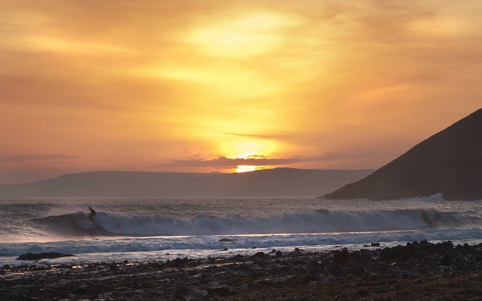 Surfer riding a wave at sunset with a mountain backdrop