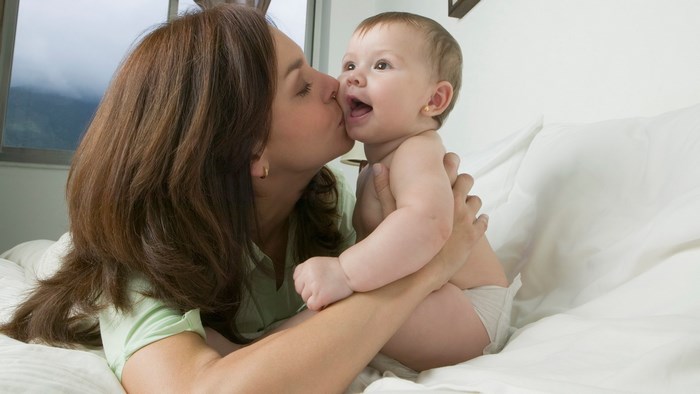Mother kissing baby on bed