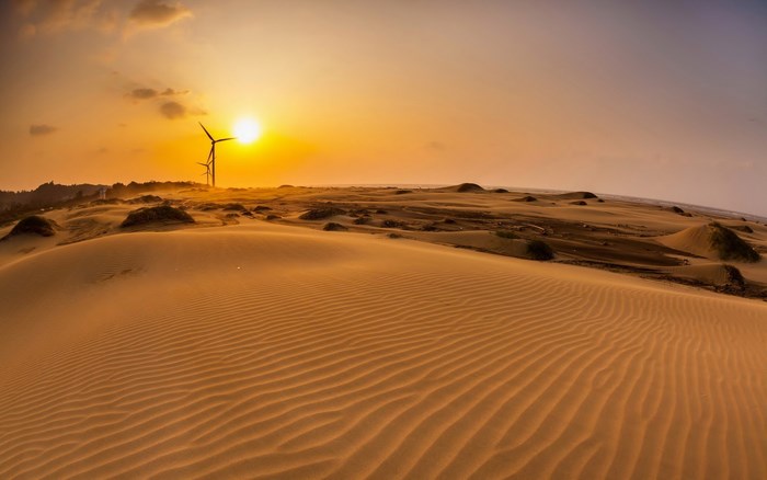 Desert dunes with wind turbines at sunset