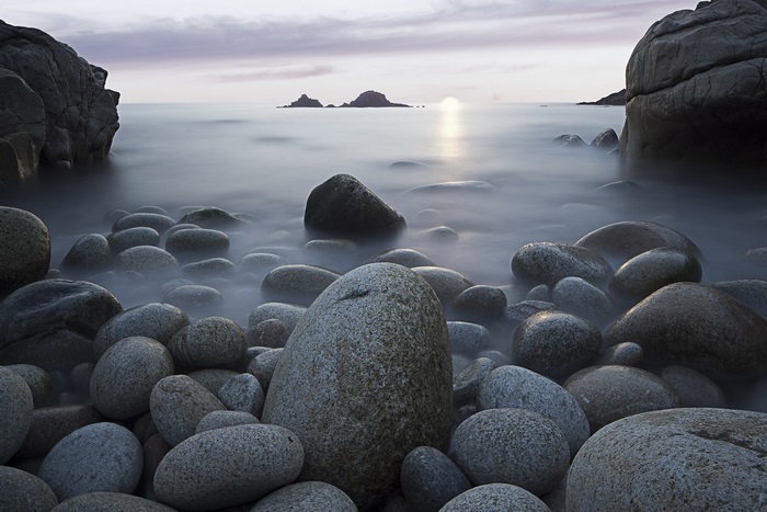 Pebble beach with calm ocean and rocky islands at sunset
