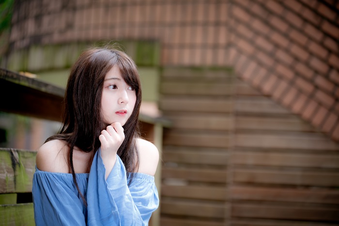 Asian girl in blue off-shoulder top sitting outdoors
