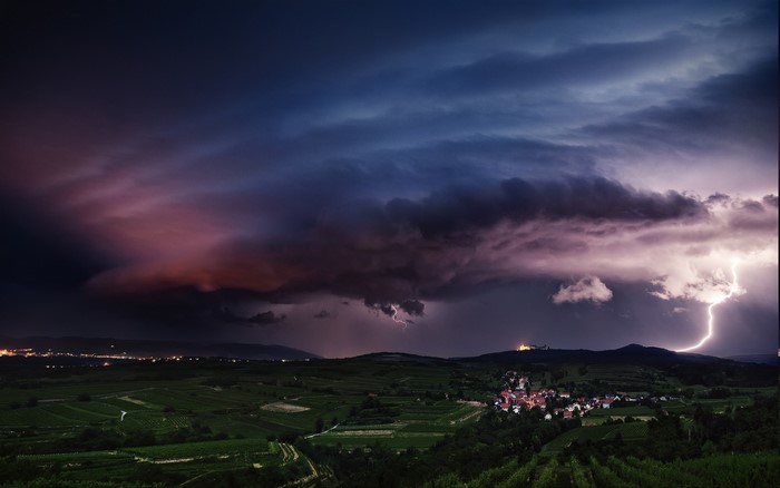 Lightning storm over a village and vineyards at night