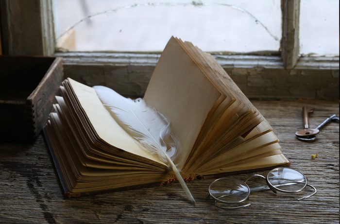 Vintage book with feather and glasses on wooden table
