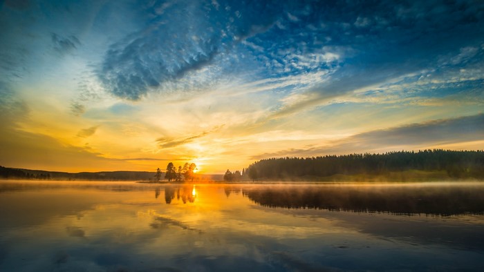 Sunrise over a misty lake with forest reflection