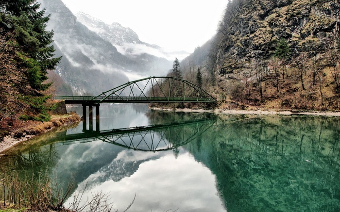 Green bridge over a lake with mountains