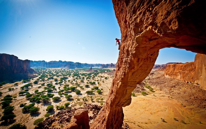 Rock climber on a natural arch in a desert landscape