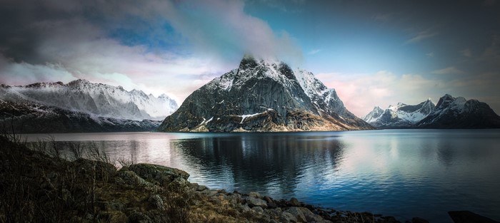 Snowy mountains reflected in a calm fjord under cloudy skies