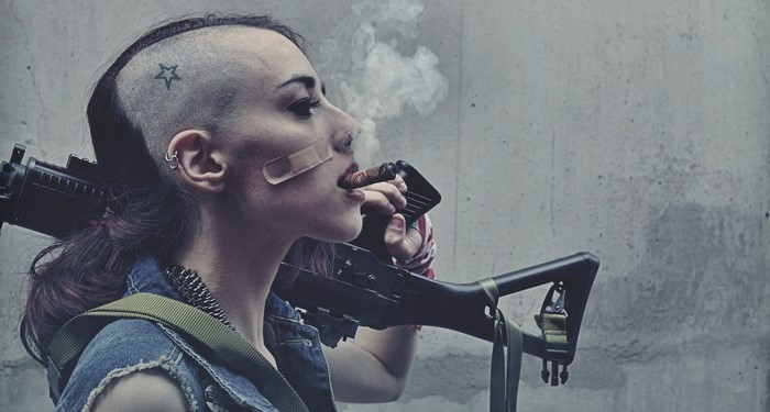 Woman with shaved head smoking cigar holding rifle