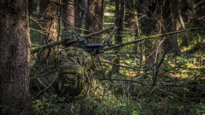 Soldier in camouflage aiming an assault rifle in a forest