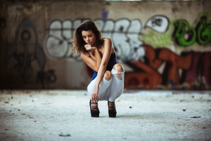 Woman in torn jeans and high heels crouching in front of graffiti