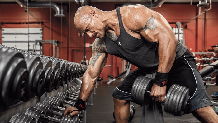 Dwayne Johnson performing dumbbell rows in a gym