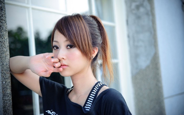 Asian woman with ponytail leaning against a wall