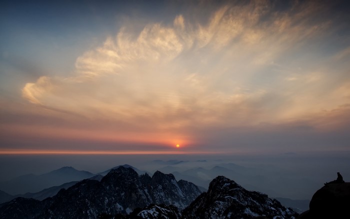 Sunset over misty mountains with a lone figure