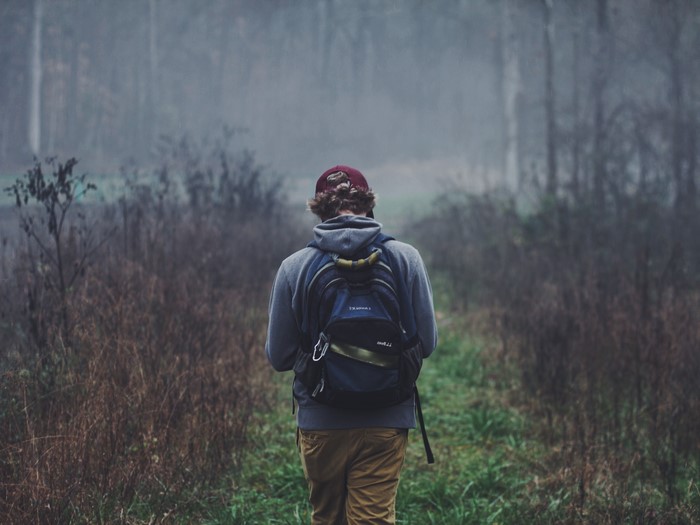 Man with backpack walking in foggy forest