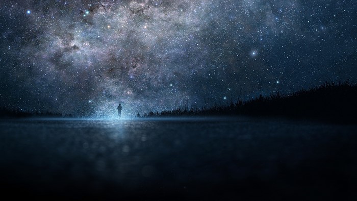 Person walking under a starry sky by a lake