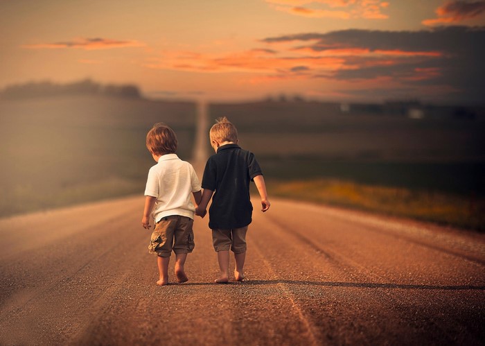 Two young boys walking on a dirt road at sunset