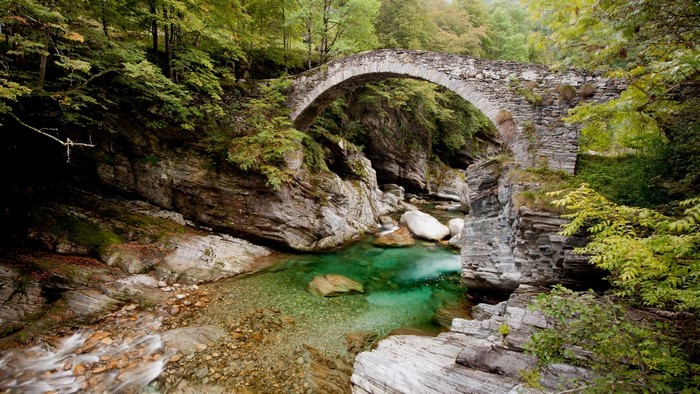 Stone bridge over a clear turquoise river in a forest