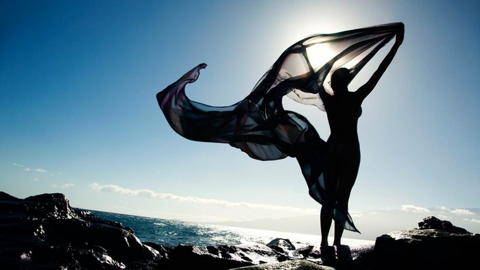 Woman with flowing fabric on rocky shore