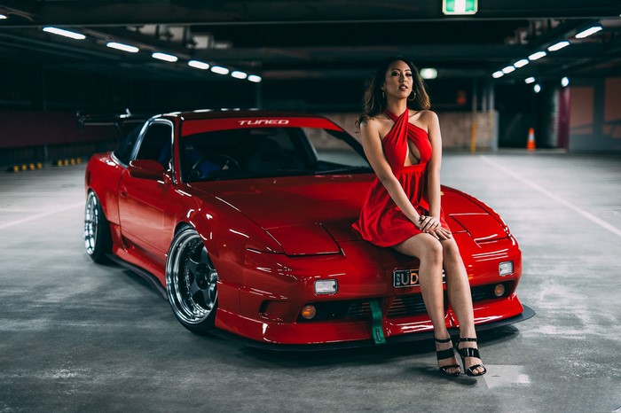 Woman in red dress sitting on a red Nissan 240SX in a parking lot