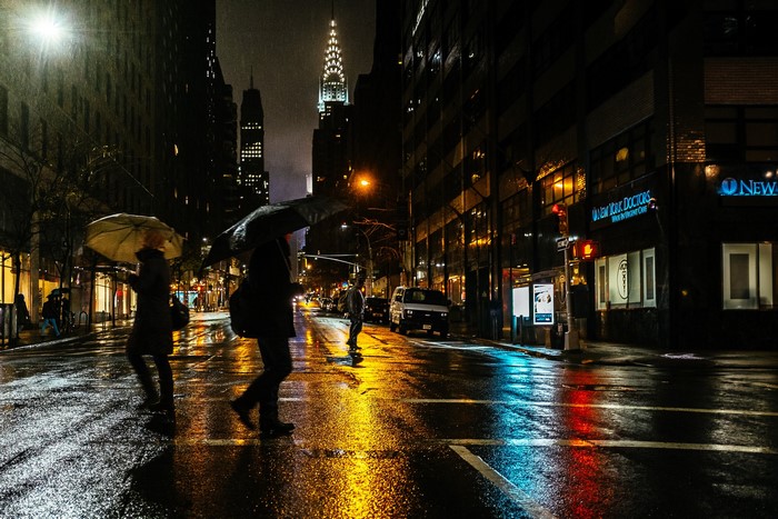 People with umbrellas crossing a wet street in New York City at night