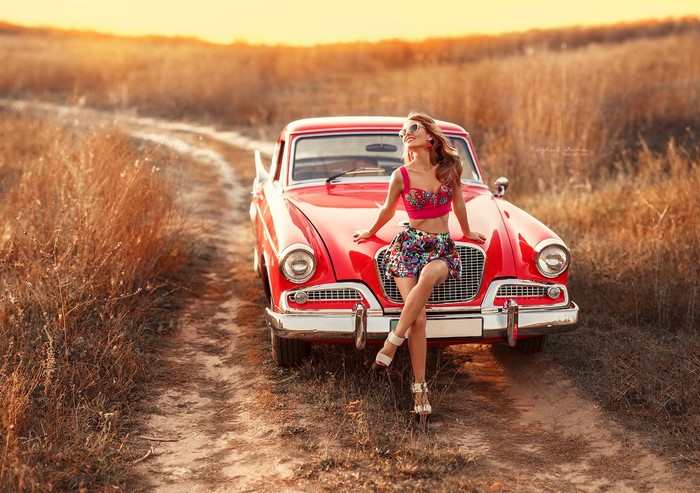 Woman posing with a vintage red car in a field