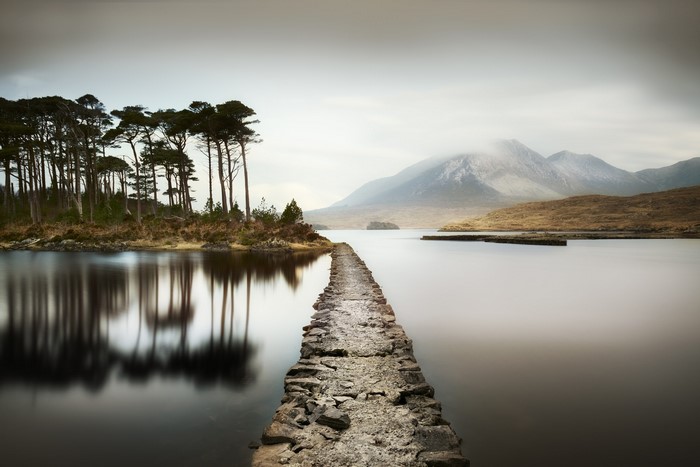 Stone path across a lake with trees and mountains