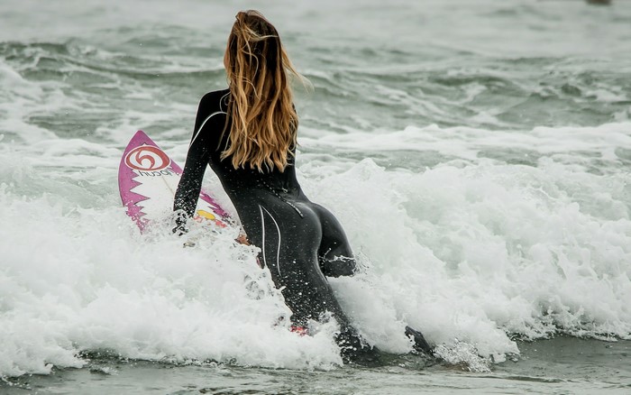 Woman in wetsuit with surfboard in ocean waves
