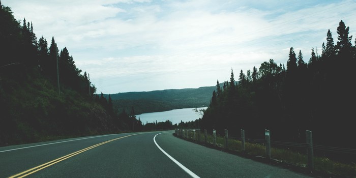 Road curving towards a lake surrounded by forests in Canada