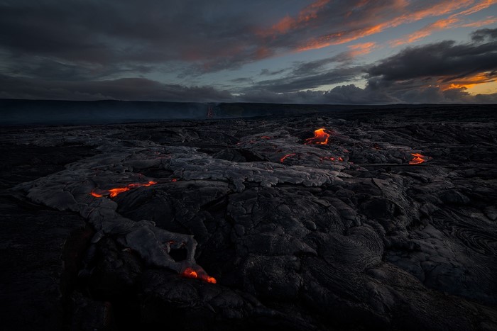 Molten lava flows across dark volcanic rock landscape at sunset