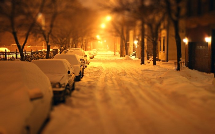 Snowy street at night with parked cars and streetlights