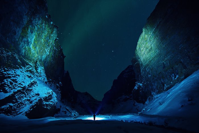 Man with flashlight in snowy canyon under aurora borealis