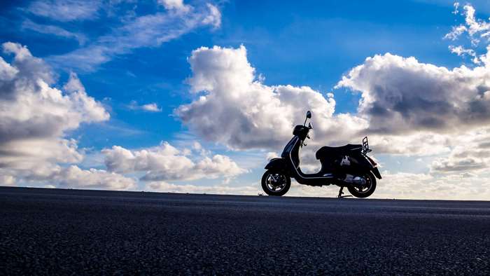 Scooter parked on a road under a cloudy sky