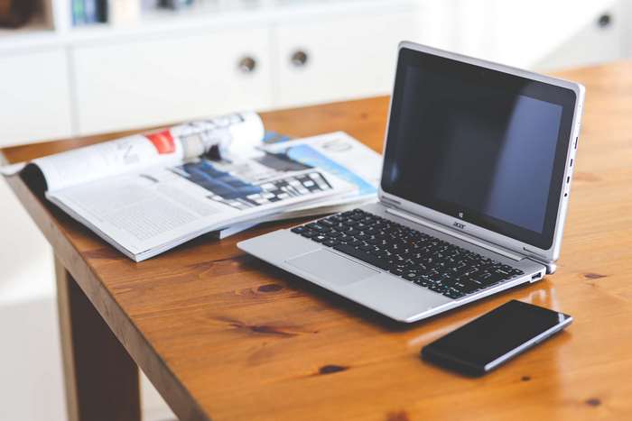 Acer laptop, magazines, and smartphone on a wooden desk
