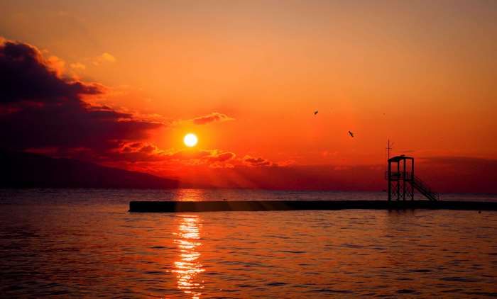 Sunset over the ocean with a pier and lifeguard tower