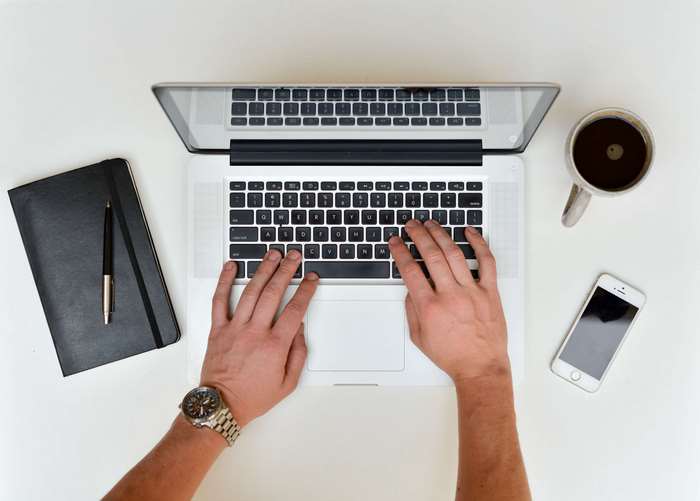 Overhead view of hands typing on a MacBook Pro with coffee and smartphone