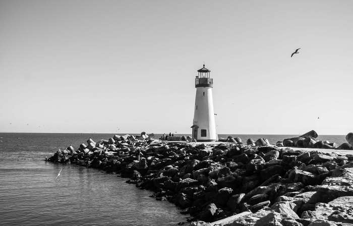 Black and white lighthouse on rocky shore with ocean