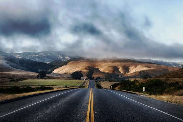 Road through rolling hills under cloudy sky