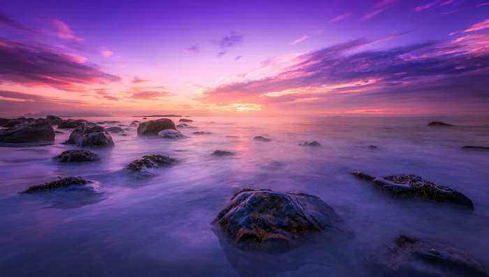 Rocky ocean shore at sunset with purple and pink sky