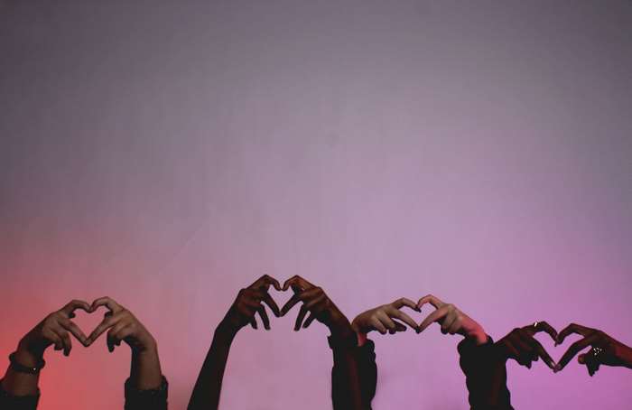Diverse hands forming hearts against a pink and purple gradient