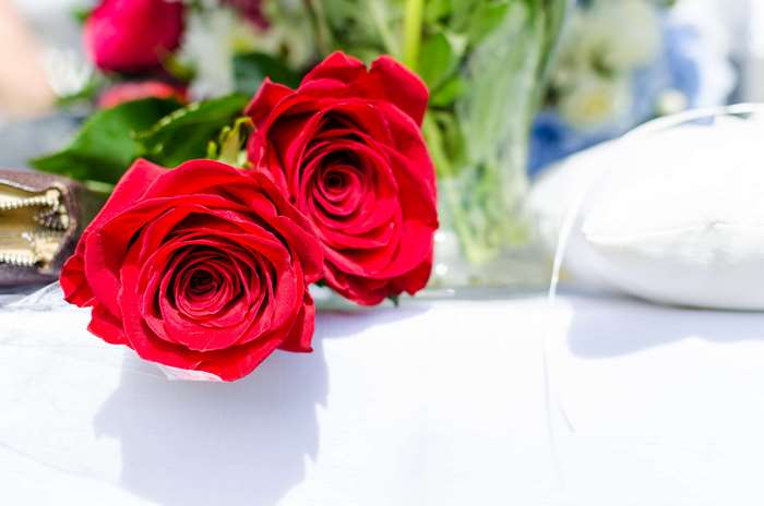 Two red roses on a white surface with a bouquet