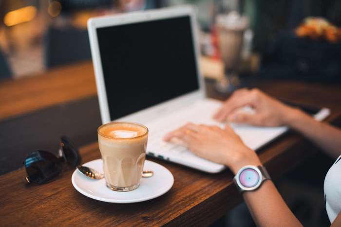 Person typing on laptop with coffee and sunglasses