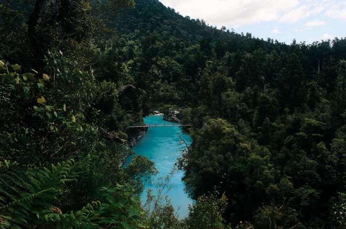 Turquoise river flowing through a dense forest with a bridge