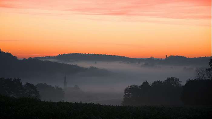 Sunrise over foggy hills with church spire