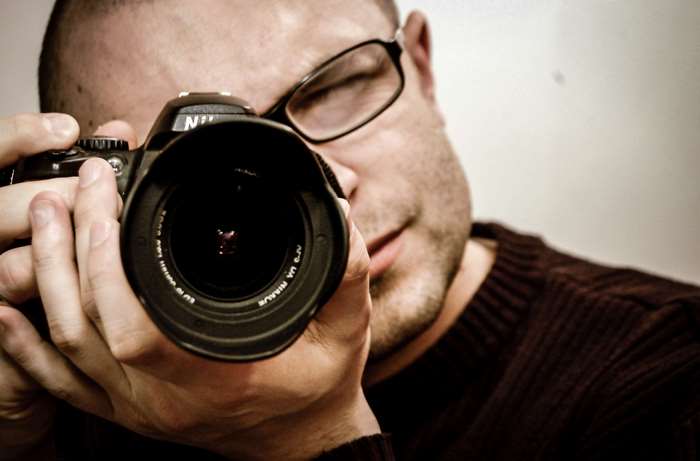 Man wearing glasses holding a Nikon camera