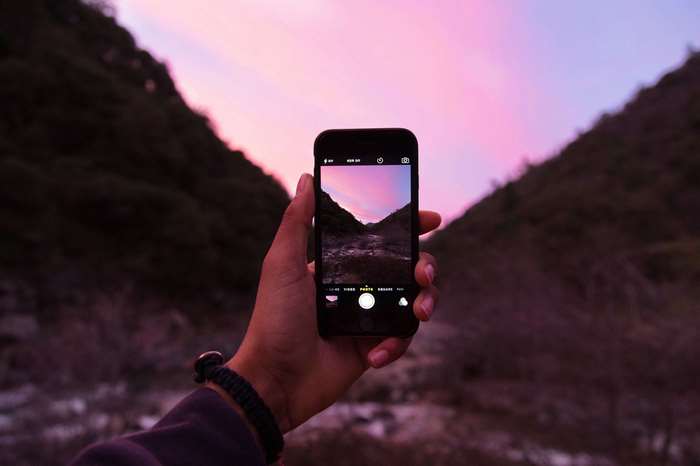 Hand holding iPhone taking photo of mountain landscape at sunset