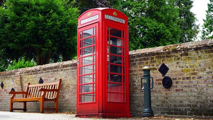 Red telephone booth next to a brick wall and bench