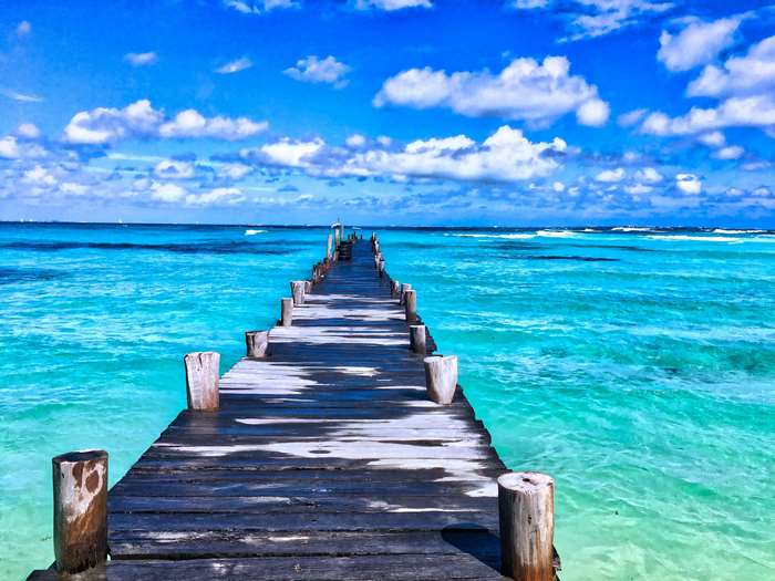 Wooden pier over turquoise ocean under blue sky with clouds