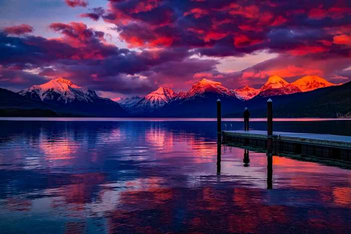 Person on dock watching sunset over mountains and lake