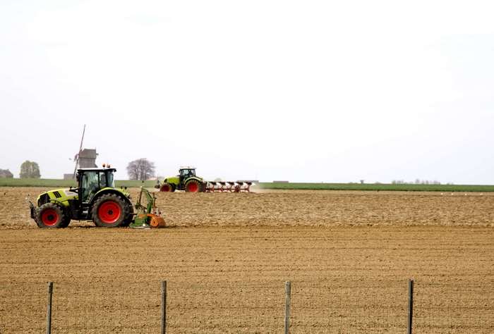 Tractors plowing a field with a windmill in the background